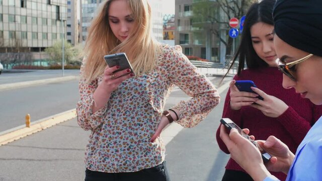 A group of girls on a busy street looking at their screens, phubbing each other, addicted to their technology. 