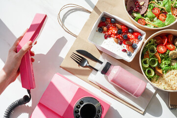 Hand of woman holding telephone receiver call to order weight loss diet fresh healthy food take away boxes, daily nutrition ready menu plan meal online delivery service ad concept. Flat lay top view