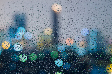 Rain drop on glass window in monsoon season with colorful bokeh light from city buildings...