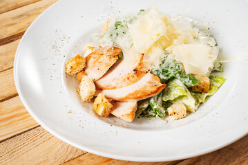 Fresh caesar salad in white plate, wooden background