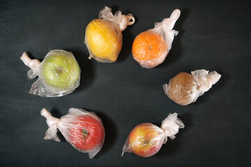 fruits, each in individual plastic package on black background, concept of environment pollution...