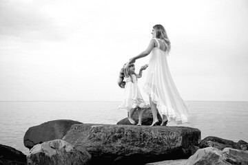 Fototapeta na wymiar black and white photo, mother and daughter dancing on big rocks, on a wild beach near the sea