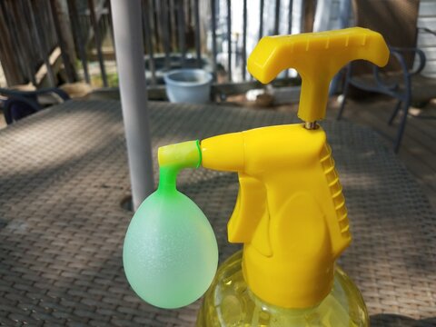 Yellow Plastic Water Dispenser Filling A Green Water Balloon