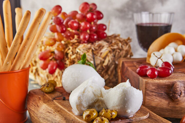 Mozzarella baby brie cheese and mozzarella mural with garlic and grapes and a glass of wine on a wooden stand on a gray-blue background