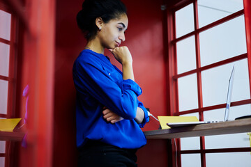 Pensive black model with smile on face standing indoors in red cabine.