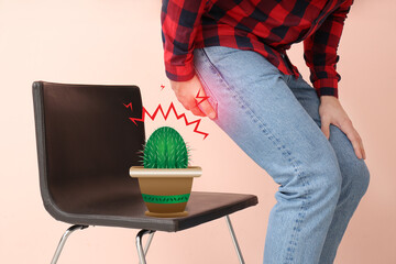 Young man and chair with drawn cactus on color background. Hemorrhoids concept
