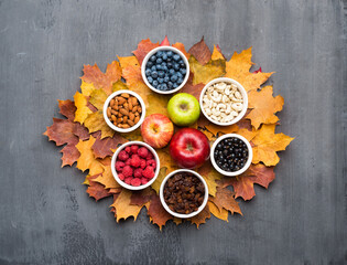 Seasonal autumn background. Frame of colorful maple leaves, raisins, nuts and berries over grey