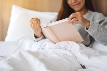 Closeup image of a beautiful young woman reading book in a white cozy bed at home