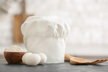 Chef's hat, utensils and products on table in kitchen