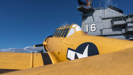Yellow T 6 Texan training prop plane on WW2 era Lexington aircraft carrier flight deck in Texas with control tower in background.