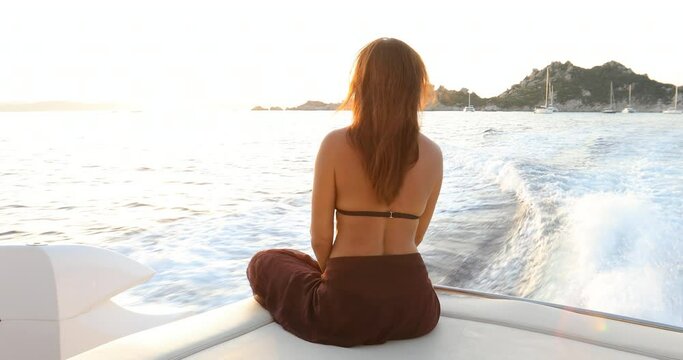 SLO MO MS Rear view of woman sitting on yacht deck at sunset / La Maddalena island, Sardinia, Italy