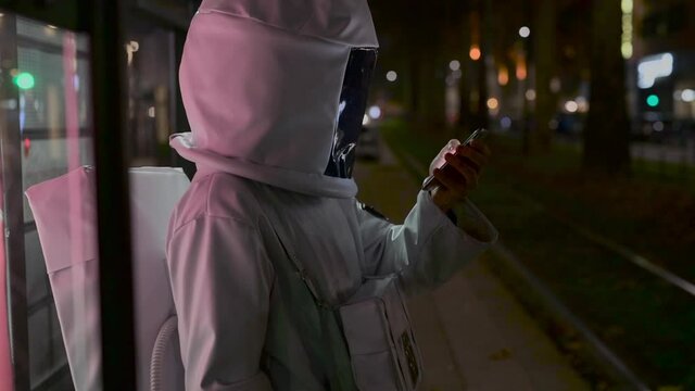 MS Man in astronaut costume with smart phone on tram stop at night/ Milan, Italy