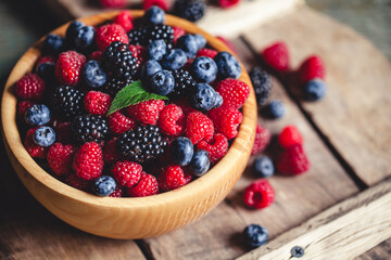 blueberries and raspberries, blackberry in a wooden bowl on old wood background