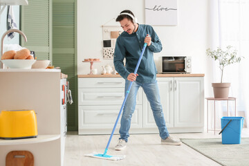 Handsome young man mopping floor in kitchen