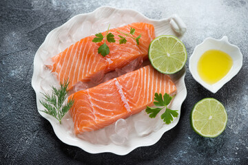 Shell-shaped plate with raw iced salmon fillet and seasonings over dark-grey stone background, horizontal shot