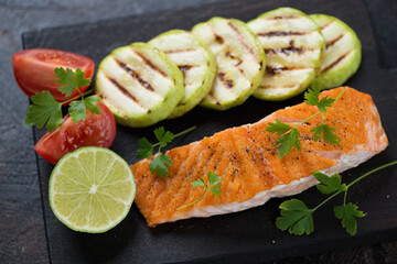 Grilled salmon fillet with zucchini slices, tomatoes, lime and fresh parsley, selective focus, horizontal shot