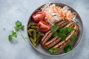 Grey plate with fried sausages, sauerkraut, gherkins, tomatoes and parsley, studio shot on a light-blue stone background
