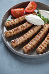 Closeup of grilled serbian cevapi or cevapcici sausages with kajmak cheese, green onion and tomatoes, selective focus, vertical shot