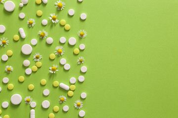 Pills with chamomile flowers on color background