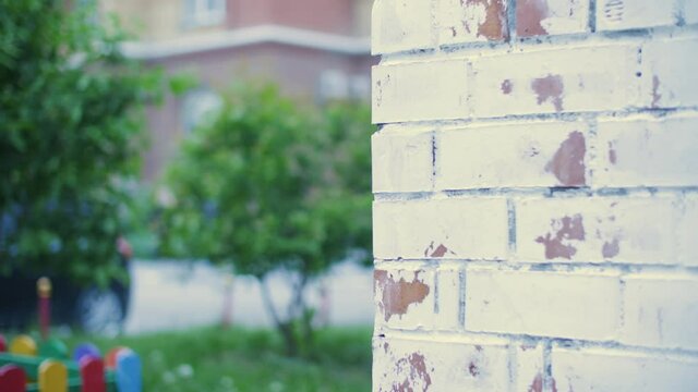 Scared girl teenager peeping out from brick house corner in residential district. Worried girl hiding around house corner in residential area