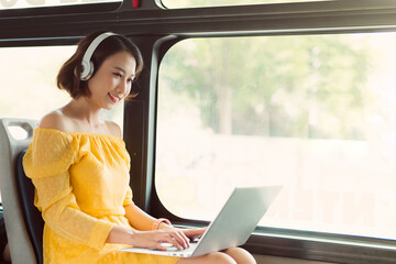 Young businesswoman using laptop and listening to music when sitting on the bus.