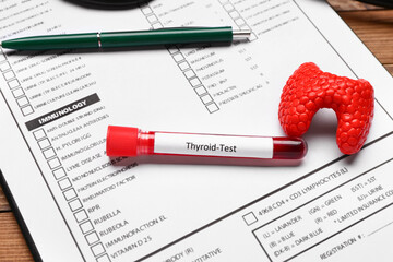Blood sample in tube with model of thyroid and laboratory test form on table, closeup