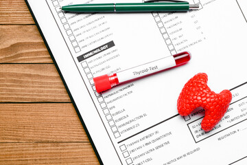 Blood sample in tube with model of thyroid and laboratory test form on wooden background