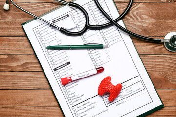 Blood sample in tube with stethoscope, model of thyroid and laboratory test form on wooden background