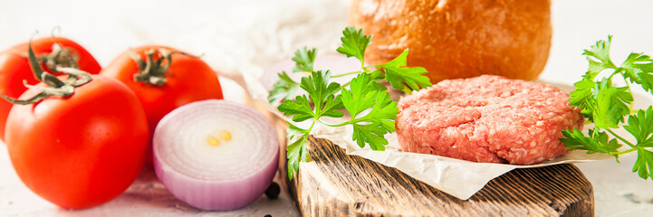 Raw Ground beef meat Burger steak cutlets with seasoning, cheese, tomatoes, and bun on vintage wooden boards, selective focus. copy space