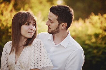 Fototapeta premium A guy and a girl kiss and walk in nature among the trees. Late evening romantic date at sunset.