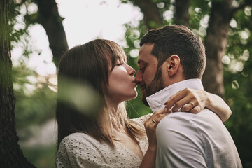 Fototapeta premium A guy and a girl kiss and walk in nature among the trees. Late evening romantic date at sunset.