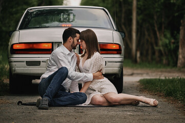 A guy and a girl are sitting in front of a car at sunset. Romantic date.
