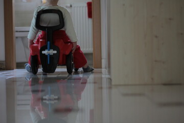 Small kid, child on a red car toy. Driving in the room alone.