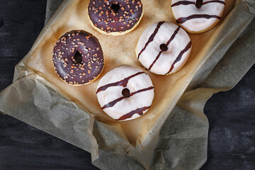 Donuts with white and brown chocolate glazing and nut sprinkles on tray with baking paper on dark background