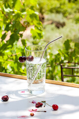Glass of cold refreshing drink or lemonade with cherry fruit on white table on summer nature background