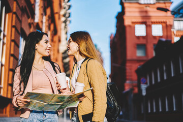 Two hipster girls discussing route of future travel sitting outdoors in urban setting