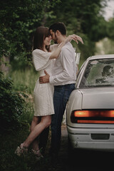 A guy and a girl are hugging next to a car. Romantic date evening walk. The relationship between people is love and tenderness.