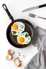 Fried eggs on frying pan on white desk top-down