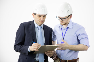 Head of project and chief engineer in hard hats discuss new project while making notes on clipboard, making calculated engineering decisions isolated on white background. Architectural project