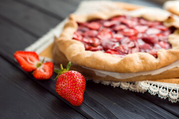 Close-up view of fresh strawberry on wooden black table on a background of baked pie with berries. Delicious traditional homemade pie. Housework. Copyspace. Flat lay. Daylight