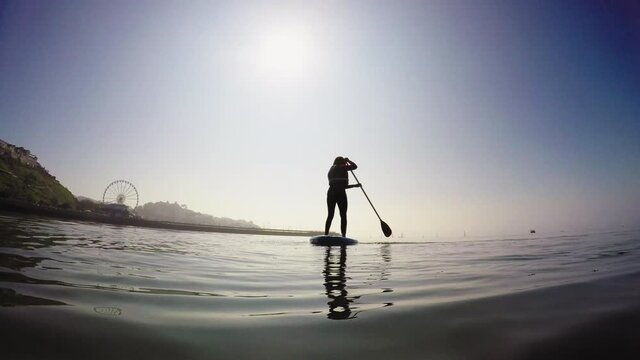 WS Rear view of woman paddle boarding on lake / Torquay, Devon, UK