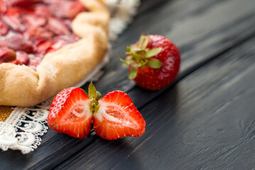 Close-up view of fresh strawberry on wooden black table on a background of baked pie with berries. Delicious traditional homemade pie. Housework. Copyspace. Flat lay. Daylight