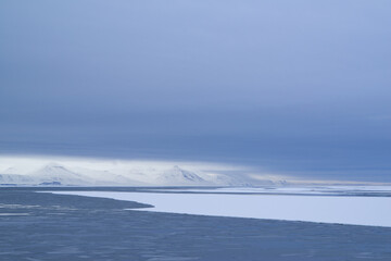 Melting sea ice in the Arctic on Spitsbergen. Mountains and clouds in white and blue at the horizon.