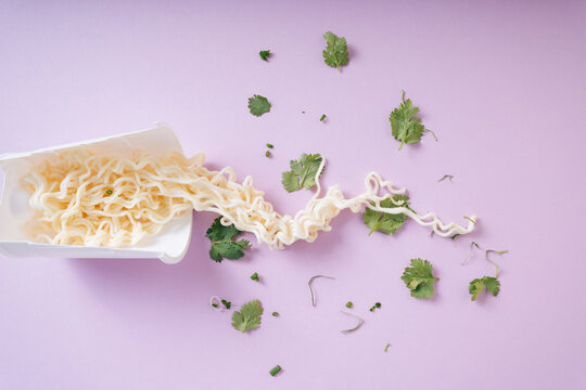 Instant noodles in white cup with parsley on purple pink background.