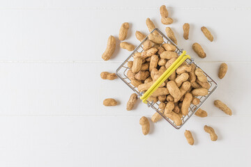 Peanuts in a grocery basket on a white wooden table. The view from the top.