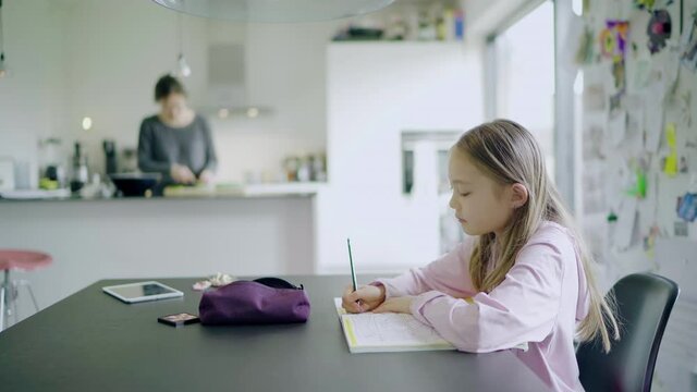 MS Girl (8-9) doing homework in kitchen, mother in background / Denmark