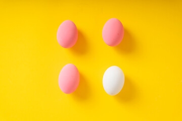 Top view - Three pink eggs and white one over yellow background.