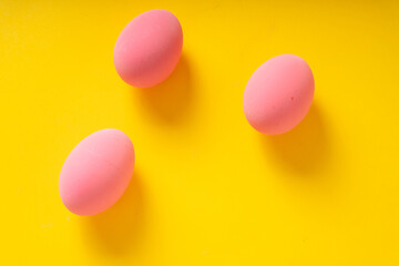 Top view - Three pink eggs over yellow background.