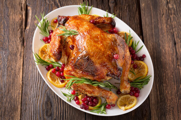 Thanksgiving Day traditional dish baked turkey. Roasted turkey or chicken with orange slices in plate for Christmas dinner on dark rustic background, top view, close up