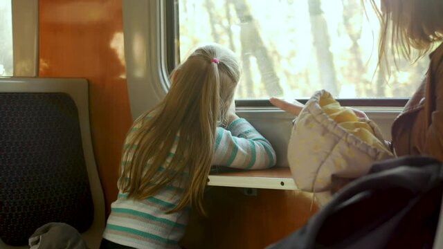 Mother and daughter travel. Cute little child girl smiles and looks out window of train in carriage during journey. Yellow trees and leaves background. Freedom concept, enjoy autumnal nature